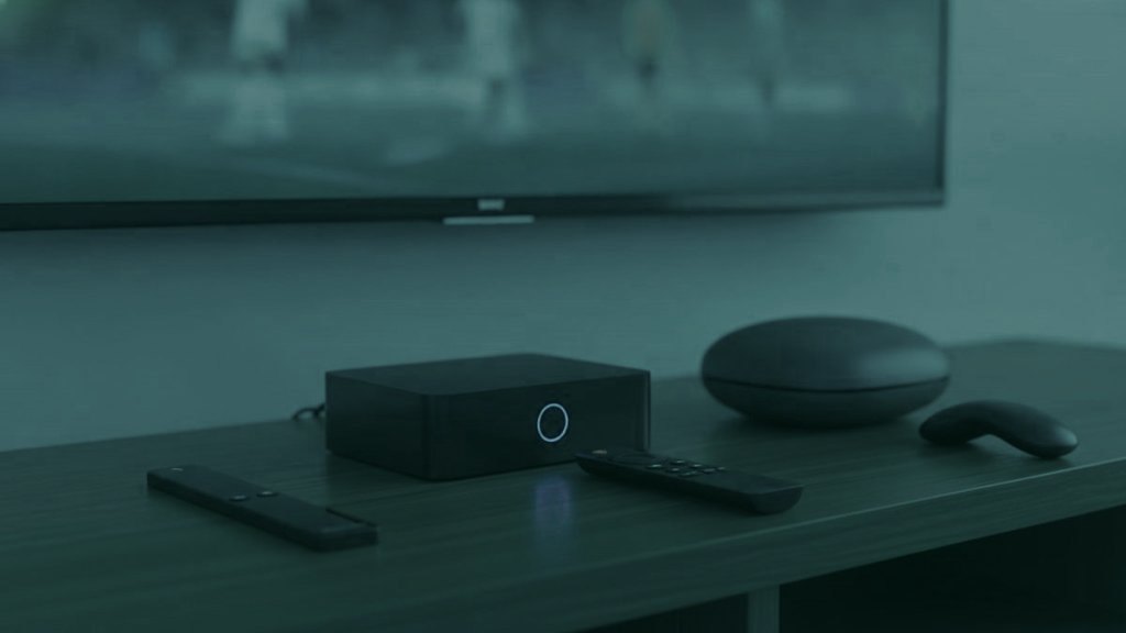 A streaming stick, a set-top box and a round streaming box with their remotes on a TV console