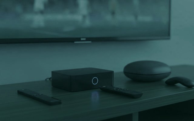 A streaming stick, a set-top box and a round streaming box with their remotes on a TV console