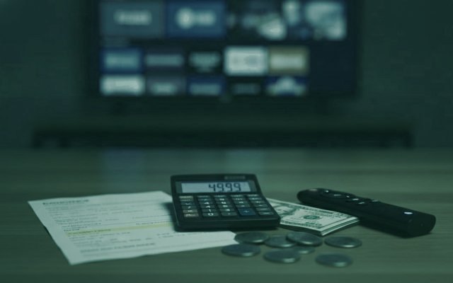 A calculator, dollar bills, coins, a streaming stick and a remote on a table in front of a TV